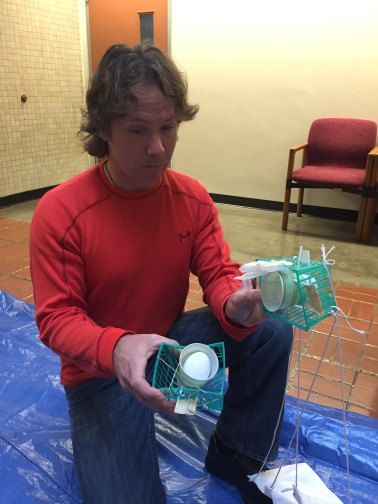Team member in red long sleeve stands with egg drop contraption in hand.